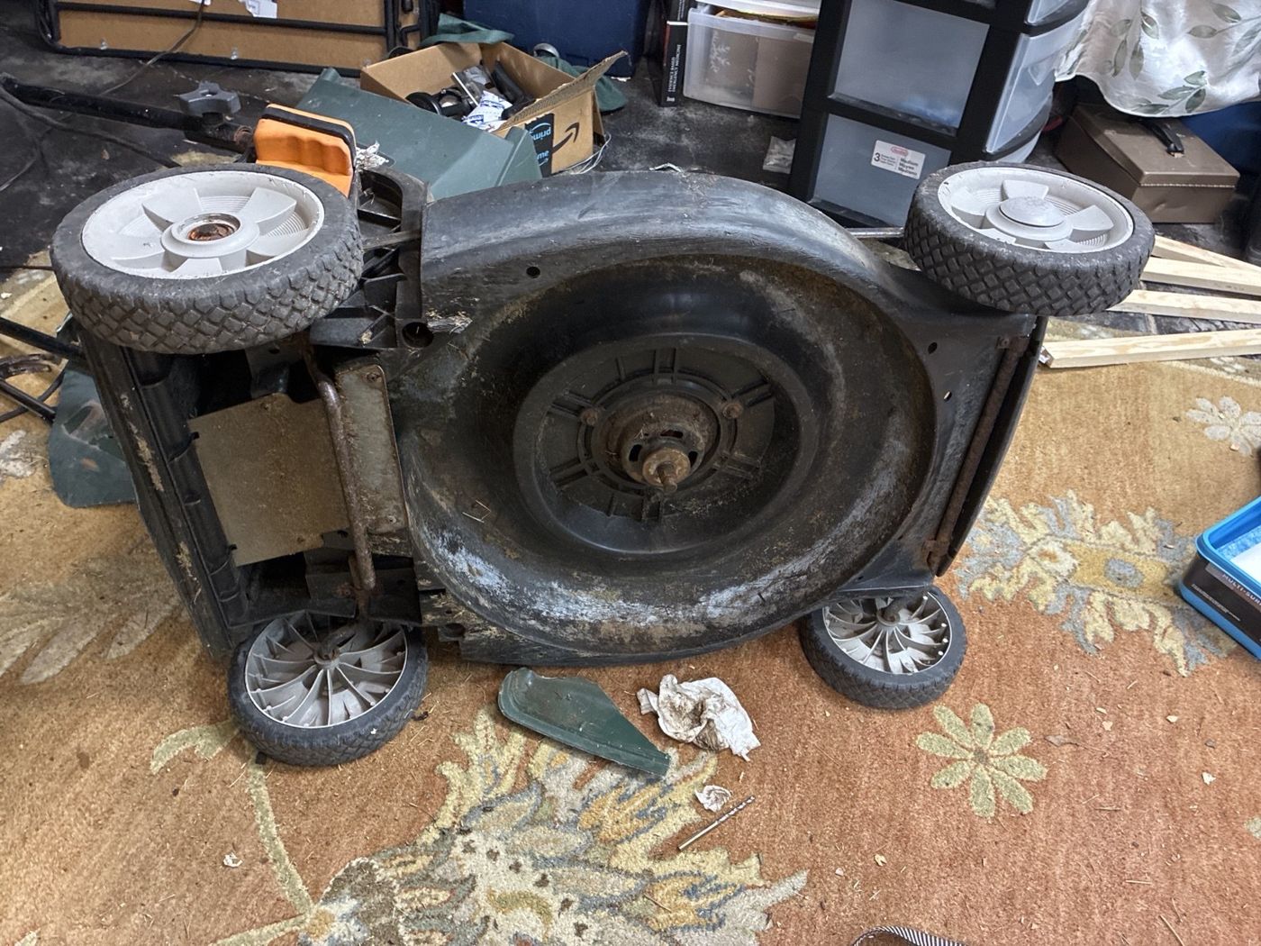 Underside of the mower showing its deck, wheel arrangement, and central blade area