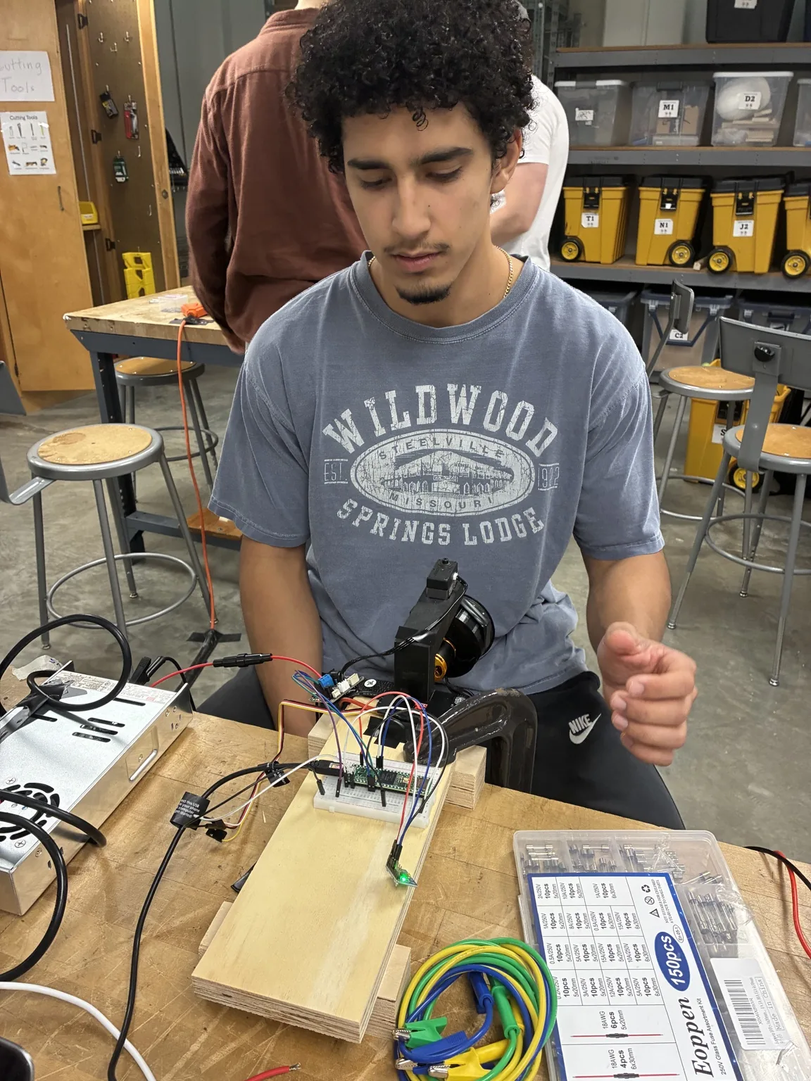 Alec assembling the thrust vector control prototype with the fan, electronics, and wooden support